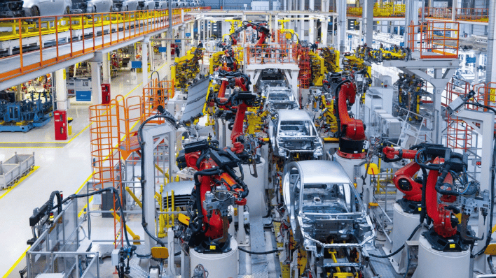 Robotic arms assembling car bodies in a brightly lit auto manufacturing plant.