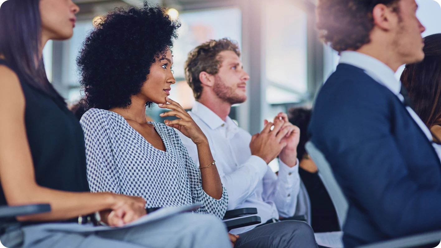 Side view of 4 employees sitting in chairs attentively listening to an unseen speaker.