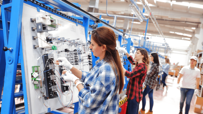 Three women in plaid shirts working on an electronics assembly line.