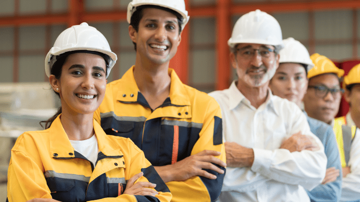Five male and female workers in hardhats with arms crossed, smiling at the camera.